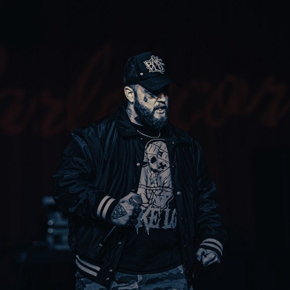 Bake Lo performing on stage in a black cap and jacket